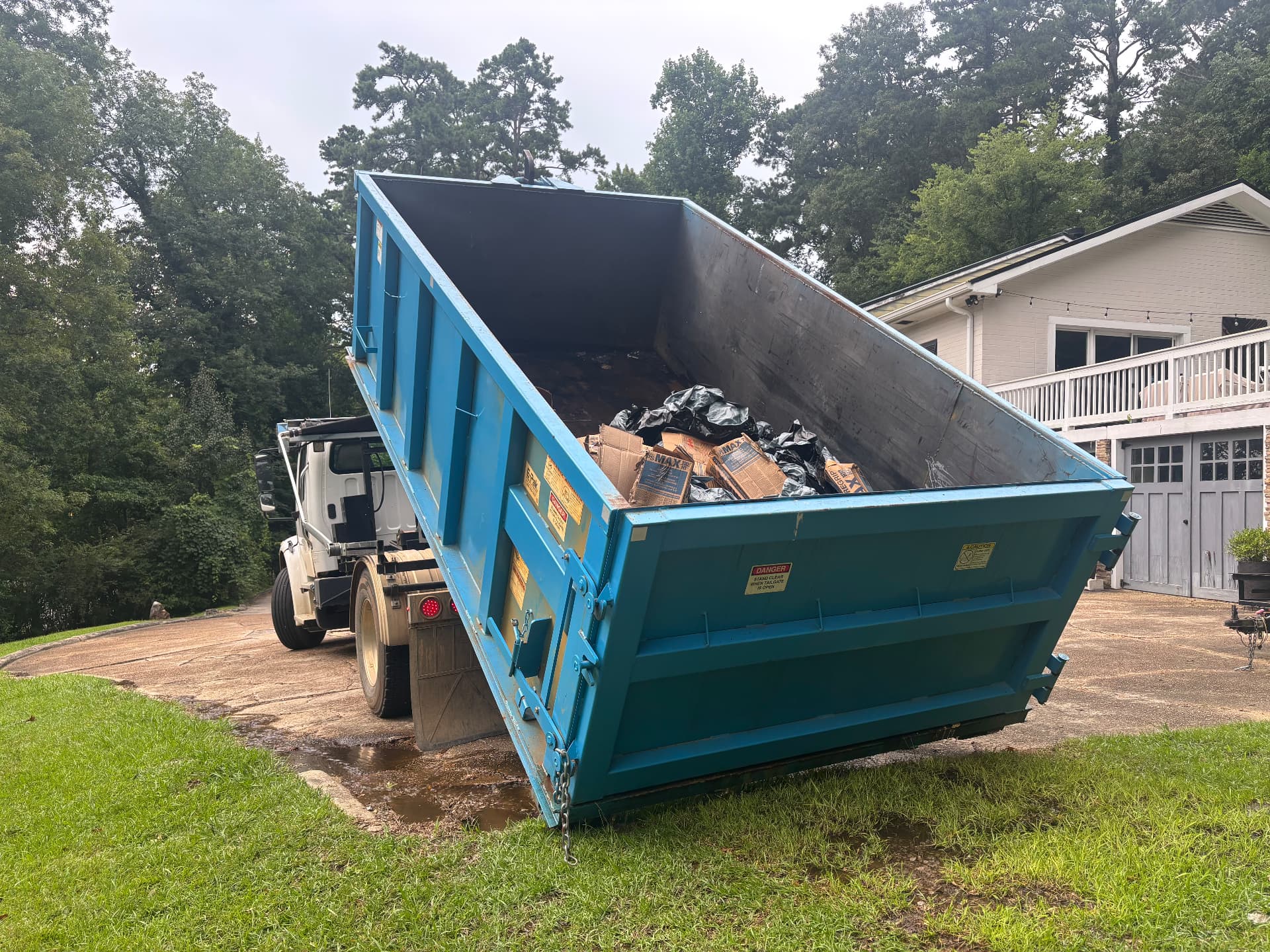 Hooklift truck loading a full roll off dumpster after a home cleanout