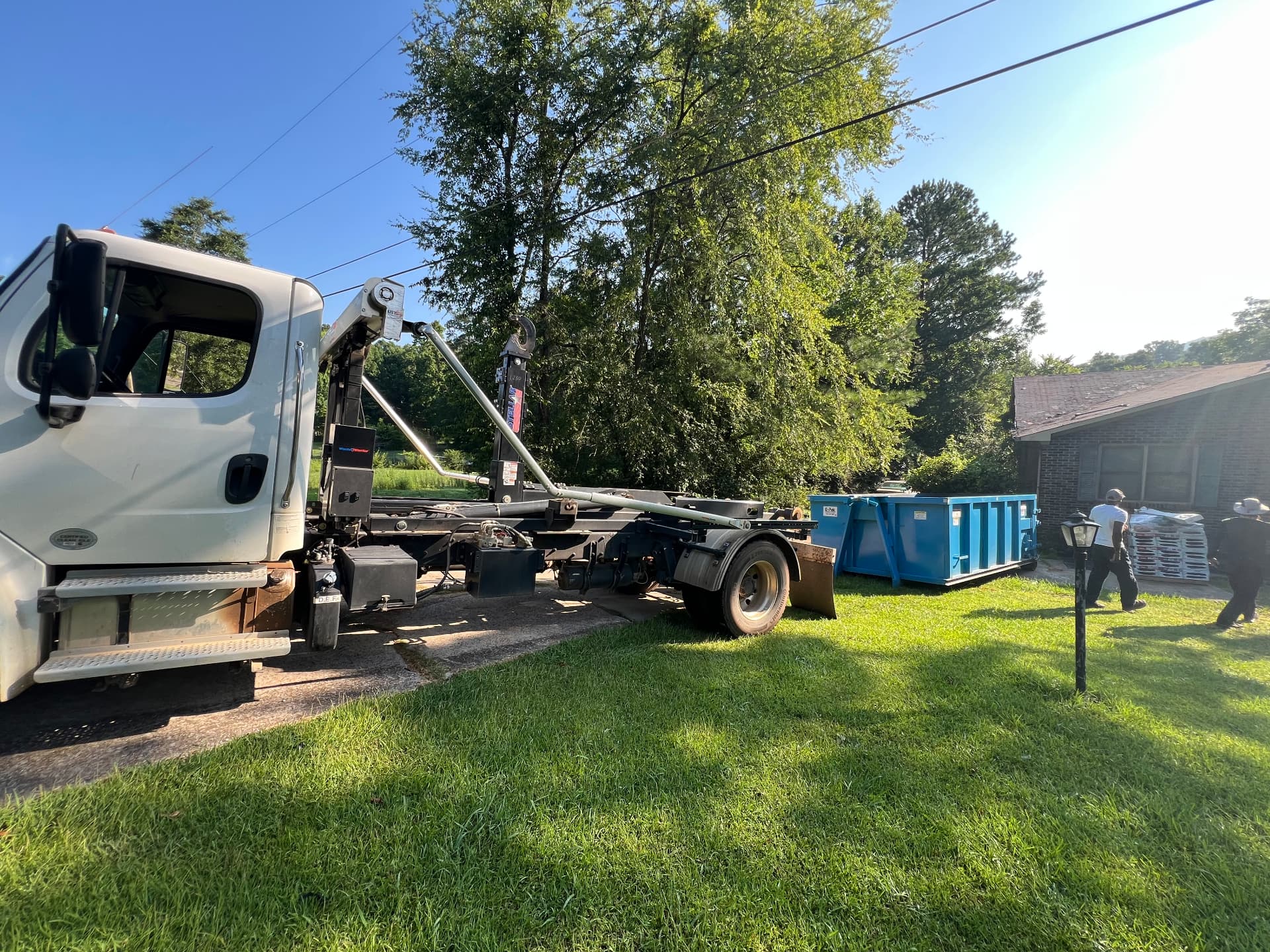 Hooklift truck parked beside a blue roll off dumpster during a residential cleanout