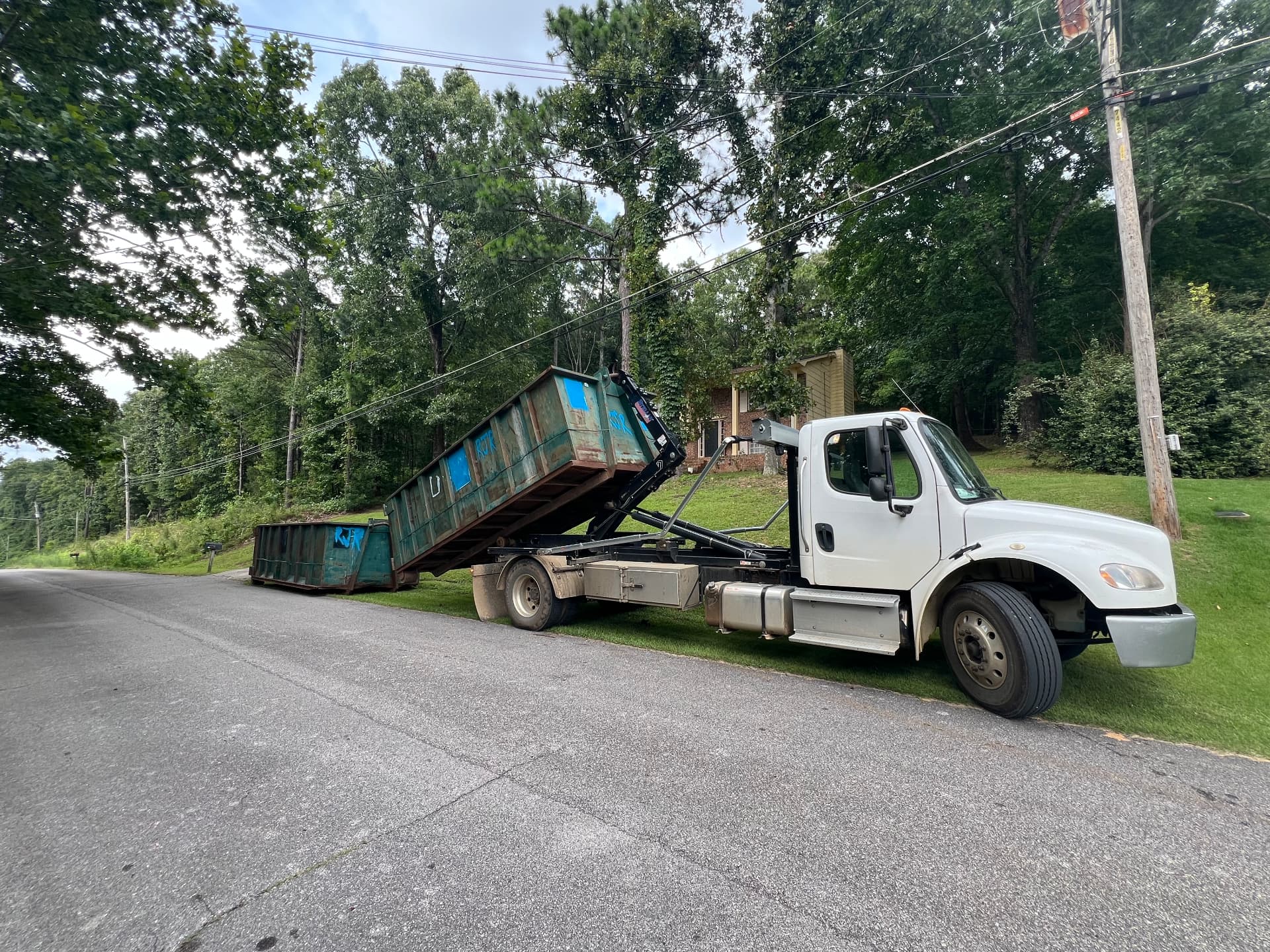 Riba Roll-Off Co. hooklift truck setting a roll-off dumpster on a residential driveway