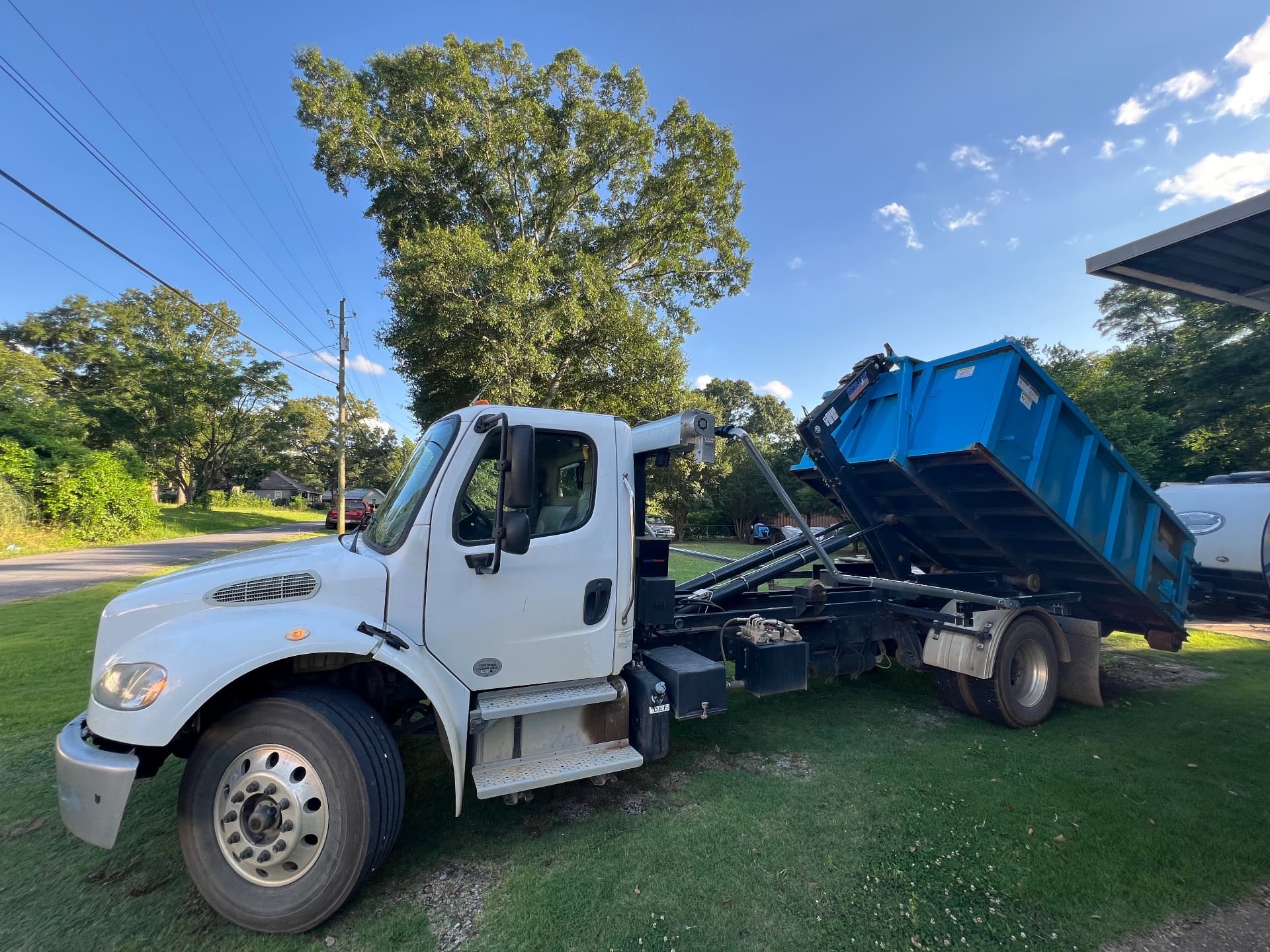 Riba Roll-Off hooklift truck tilting a blue dumpster off the frame
